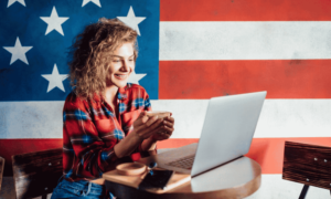 girl working on laptop behind is flag of the USA
