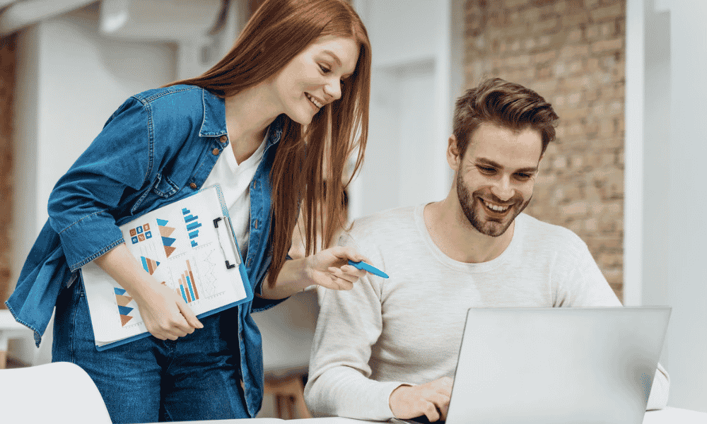 A woman and a man discussing something on a laptop in office