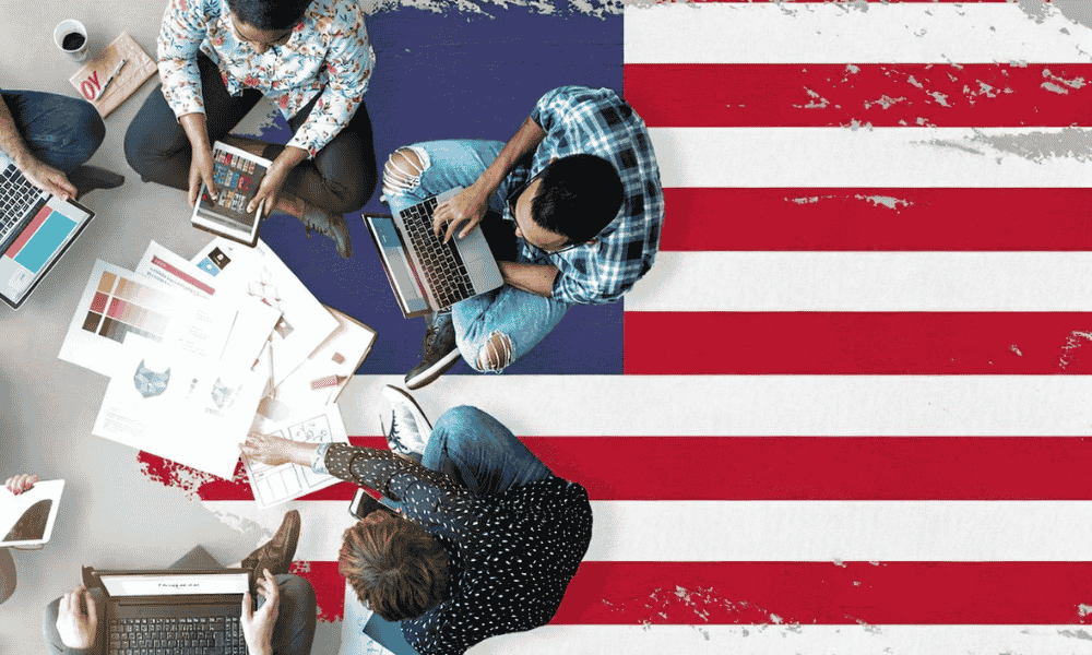 People sitting on the USA flag and working on their laptops, tabs and mobiles as well