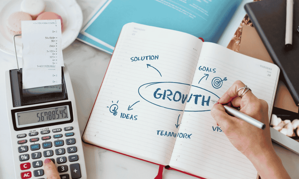 An overhead view of a hand drawing a "GROWTH" mind map in an open notebook next to a calculator with a paper receipt.